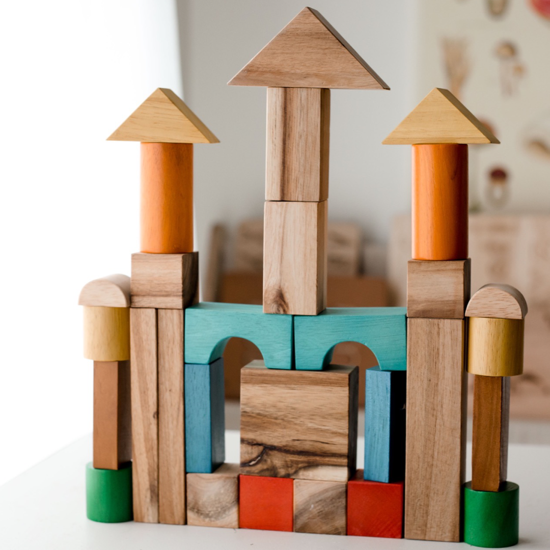 Construction display made up of the natural colour wooden blocks from QToys. Blocks are made up of triangles, semi-circles, cylinders, arches, squares, rectangles. Colours include orange, yellow, brown, blue, red, green and turquose