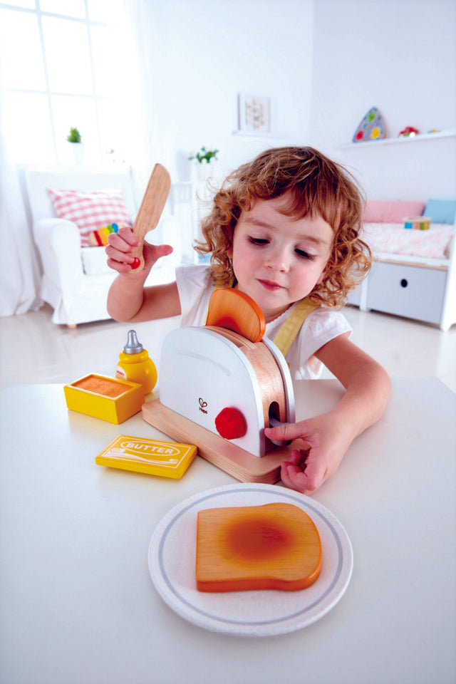 Child pushing down lever of Hape Pop-Up Toaster popping the toast out