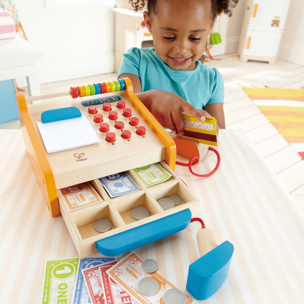 Child enjoying playing pretend swiping her credit card with cash register open showing pretend play money in till