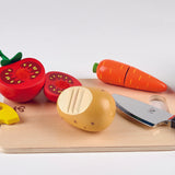 Hape cooking essentials set showing separable tomato, carrot, cheese, onion and radish on chopping board with knife, peeler and grater included.