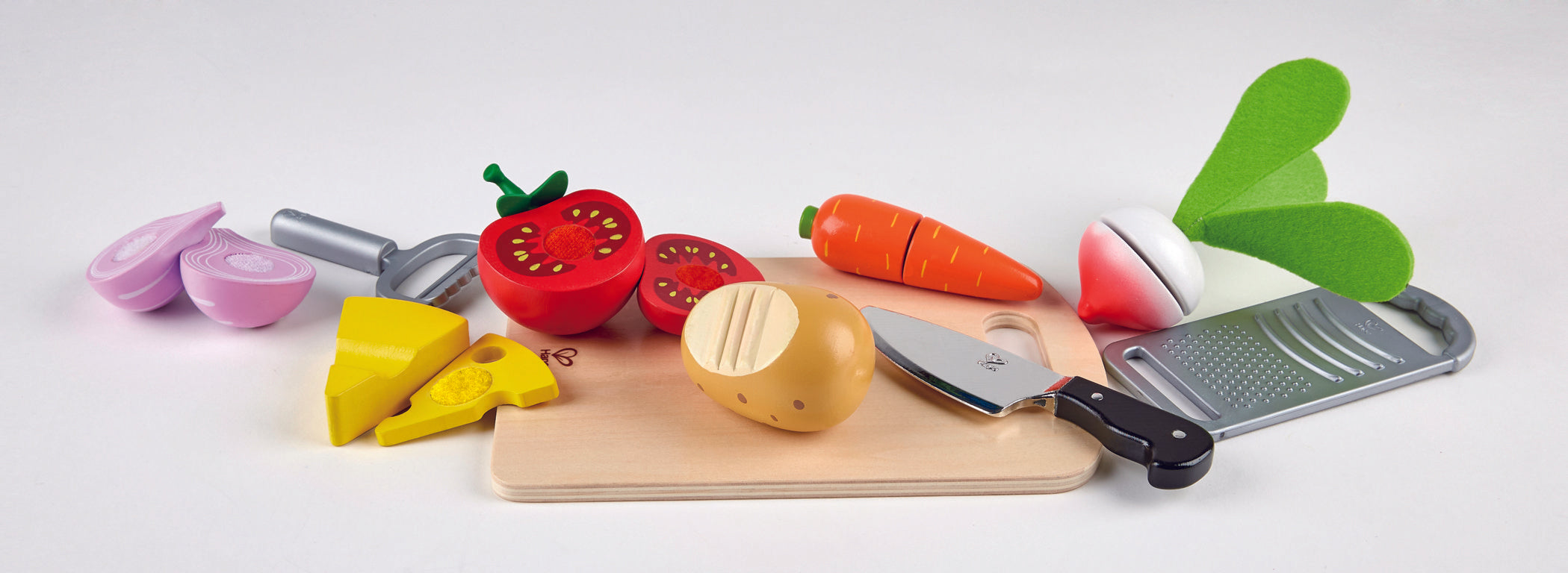 Hape cooking essentials set showing separable tomato, carrot, cheese, onion and radish on chopping board with knife, peeler and grater included.