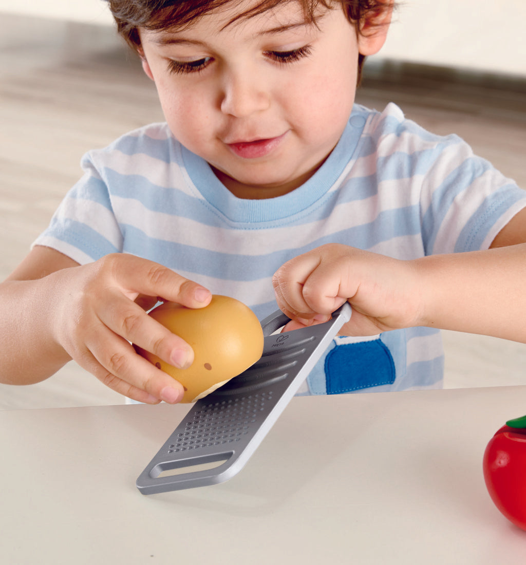 Boy grating potato on grater of Hape cooking essentials play set.