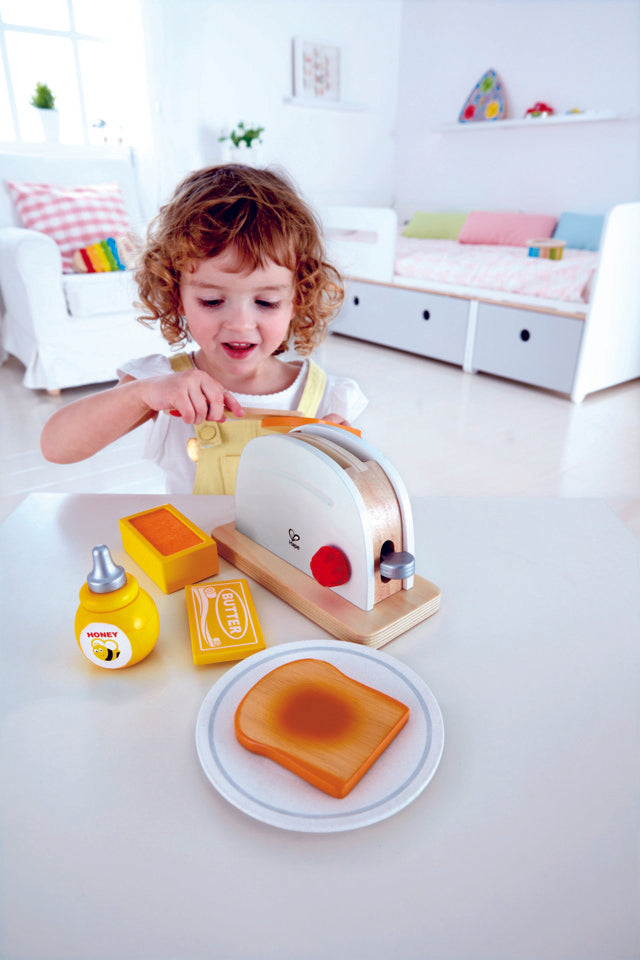Child using knife to butter piece of pretend toast from Hape Pop-Up Toaster Set