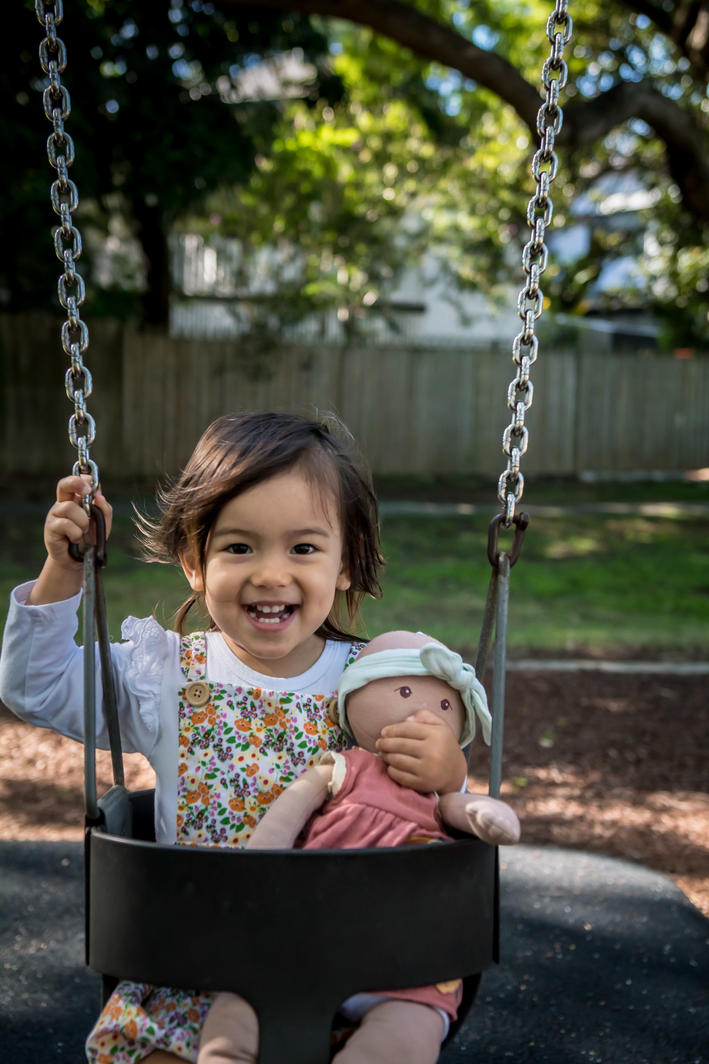 Girl on swing playing pretend with her toy baby Aria doll