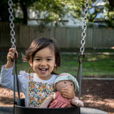 Girl on swing playing pretend with her toy baby Aria doll