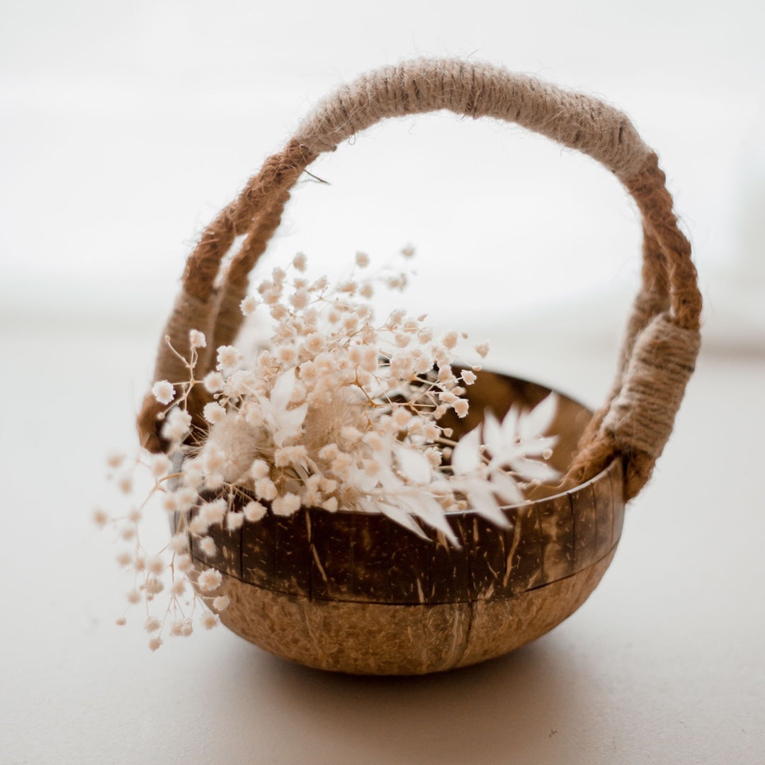 An eco-friendly coconut basket from QToys with a jute woven handle. Displayed with flowers.